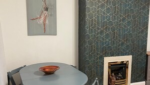 A dining area with a round table and chairs, a fireplace, and a geometric-patterned wall.