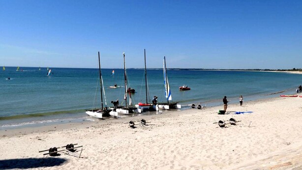 Une plage où plusieurs voiliers sont amarrés près du rivage, une plage de sable et un ciel bleu dégagé.