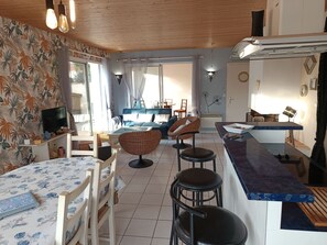 Moderni keittiö, jossa on ruokailutila, olohuone, jossa on sohva ja nojatuoleja, sekä televisio nurkassa.