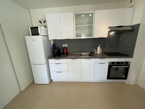 Een kleine keuken met witte kastjes, een ingebouwde magnetron, een koffiezetapparaat en een fornuis.