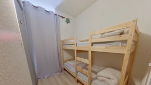 A small room with two bunk beds, a wooden floor, and a curtain.
