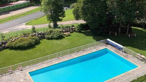 A rectangular swimming pool with a stone border, surrounded by a white fence, and a small adjacent pool.
