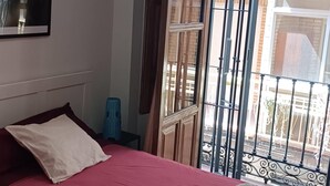 Ein Schlafzimmer mit einem Bett, einem Fenster mit Blick auf einen Balkon und einem blauen Hocker.