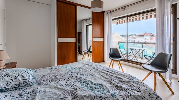 Moderni hotellihuone, jossa on suuri sänky, parveke tuoleineen ja näkymä kaupunkiin.