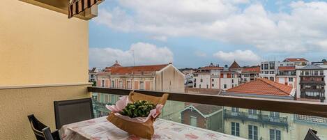 A balcony with a table covered in a tablecloth with a coffee theme, a chair, and a bouquet of flowers.