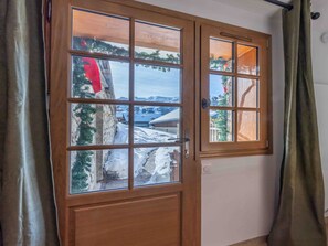 Une porte en bois avec un panneau de verre, donnant sur un espace extérieur enneigé, avec des arbres et une vue sur la montagne.