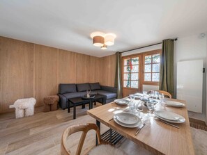 Ein modernes Wohnzimmer mit Holzboden, einer Couch, einem Esstisch für vier Personen und einem Fenster mit Vorhängen.