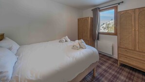 Ett hotellrum med en säng, en garderob och ett fönster med utsikt över snötäckta kullar.