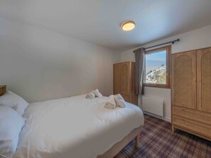 A hotel room with a bed, a wardrobe, and a window with a view of snow-covered hills. - Charming property in Méribel (Méribel)