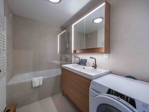 A modern bathroom with a bathtub, a sink, a mirror, and a washing machine. - Charming property in Méribel (Méribel)