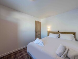 A hotel room with a wooden bed, white linens, and a plaid carpet. - Charming property in Méribel (Méribel)