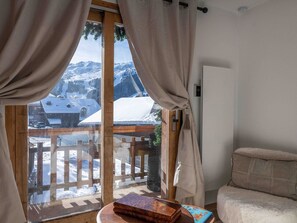 A cozy room with a wooden balcony, a plush sofa, and a view of a snowy mountain landscape. - Charming property in Méribel (Méribel)
