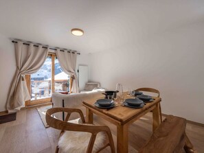 A dining area with a wooden table set for two, chairs, and a view of a snowy mountain. - Charming property in Méribel (Méribel)