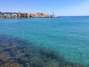 A coastal view with clear blue water, a marina with boats, and a row of buildings with balconies. - 2-room apartment with terrace near the beach (Bormes-les-Mimosas)