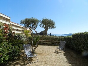 A patio area with two metal chairs, a tree, and a view of a building with multiple balconies. - 2-room apartment with terrace near the beach (Bormes-les-Mimosas)