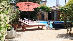 A poolside area with lounge chairs, a red umbrella, and a pool with a blue cover. - Art House in Rovinj, Croatia - Vacation Home   (Rovinjsko Selo)