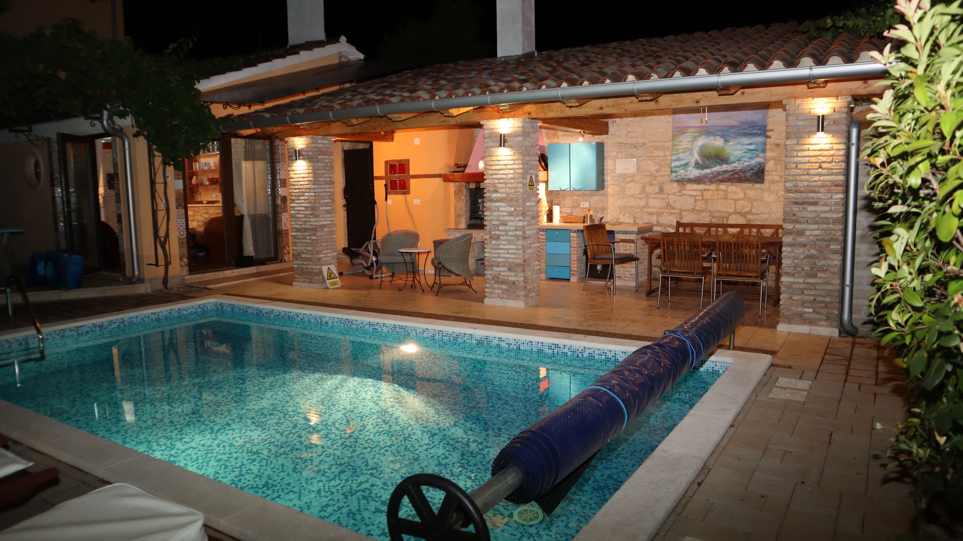 A swimming pool with a water slide, a covered outdoor seating area, and a stone wall with a painting.
