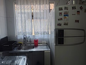 A compact kitchen with a sink, faucet, and a refrigerator. - Beach house with barbecue (Praia Grande)