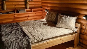 Un dormitorio de cabaña de madera con cama, lámparas de noche y una estantería con adornos.