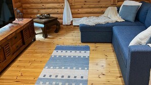 Interior acogedor de una cabaña de madera con un sofá azul, un mueble de entretenimiento de madera y vistas a la vegetación a través de una ventana.