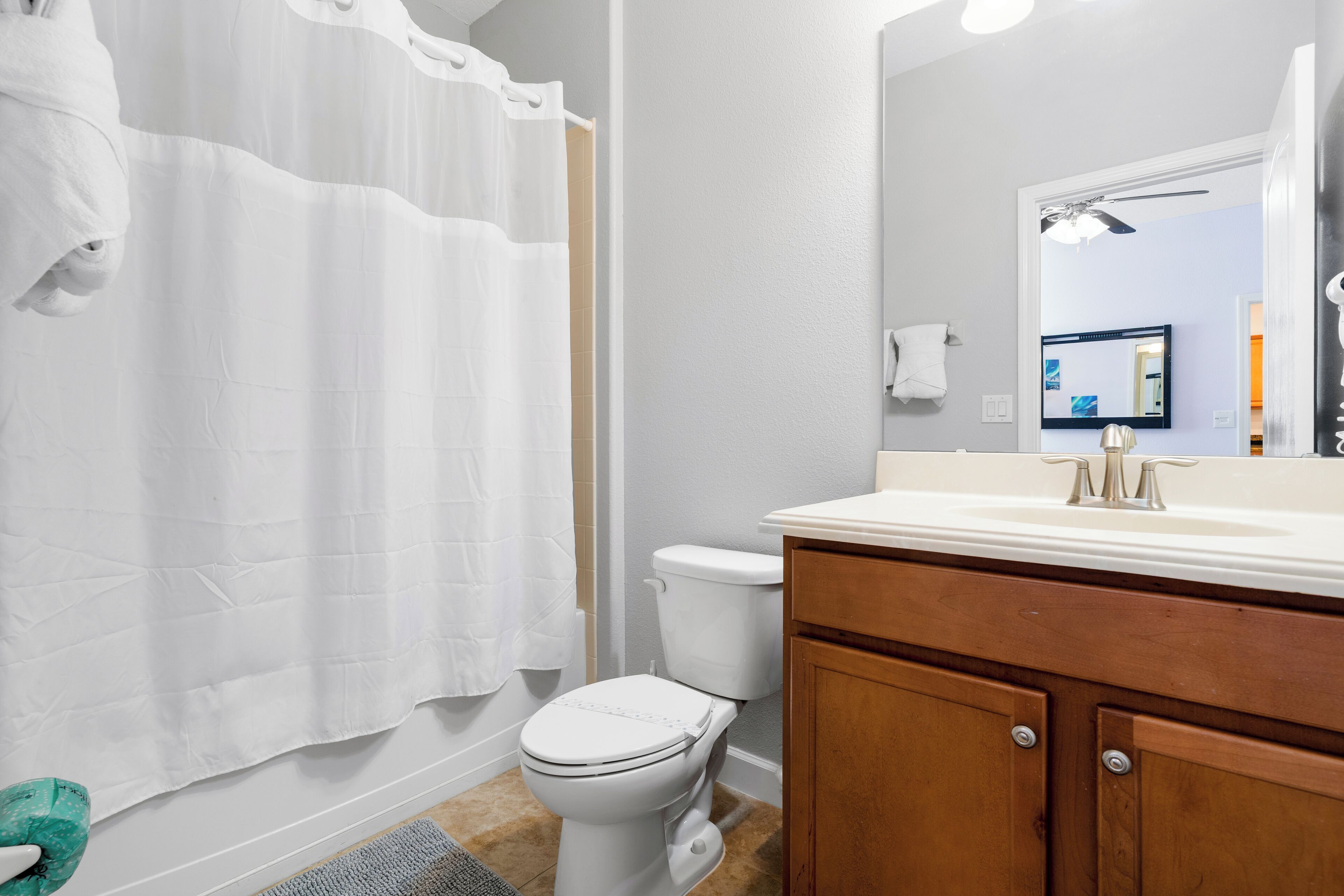 Une salle de bain avec des toilettes blanches, un meuble-lavabo en bois et un rideau de douche.