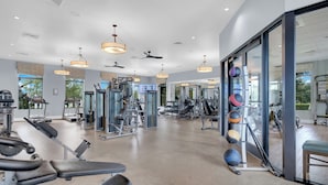 A gym with exercise equipment, large windows, and ceiling fans. - Oasis at Champions Gate: Pool, Spa & Arcade Fun! (Davenport)