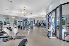Une salle de sport équipée de matériel d’exercice, dotée de grandes fenêtres et de ventilateurs de plafond.