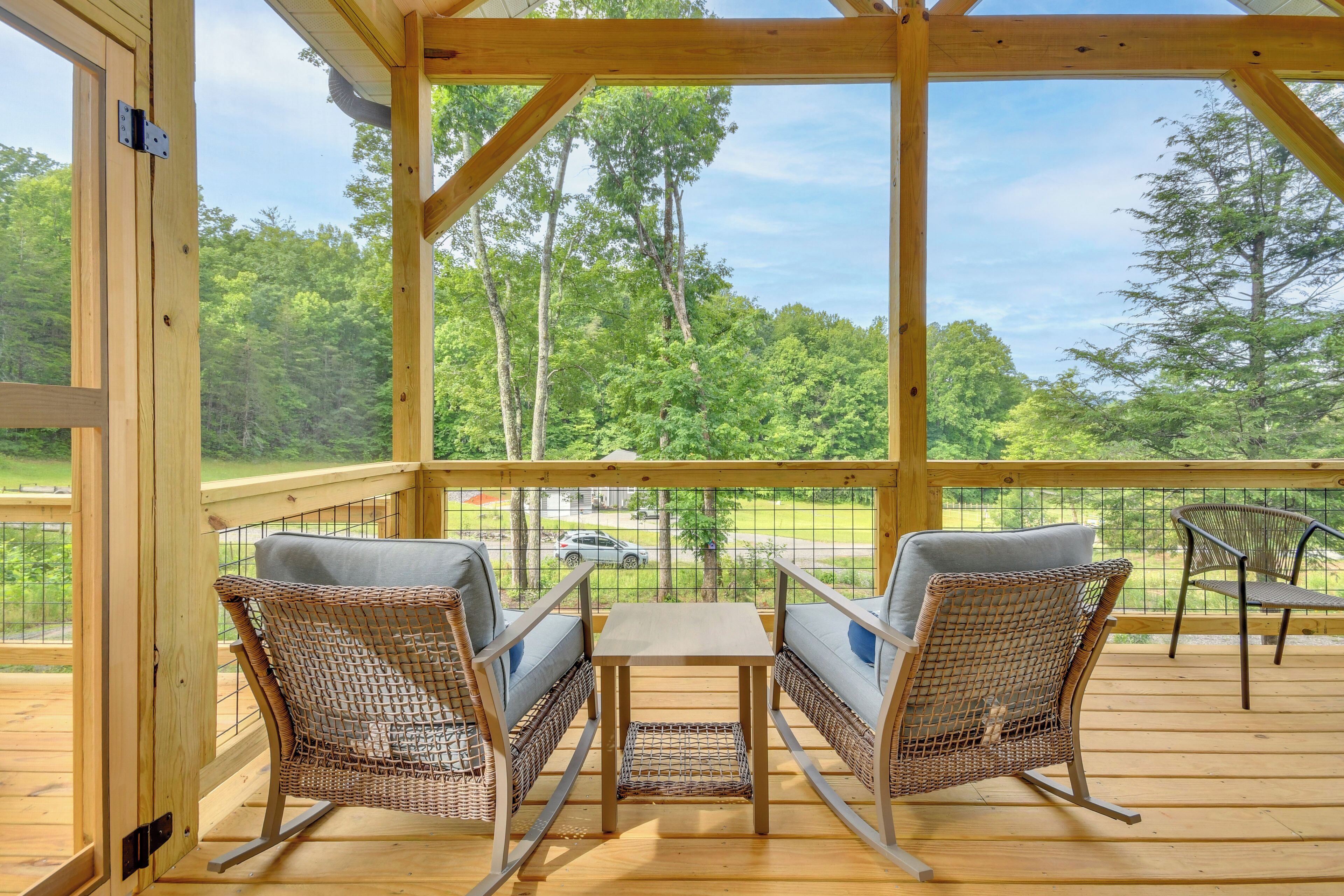 A wooden deck with wicker chairs and a table, overlooking a forested area.