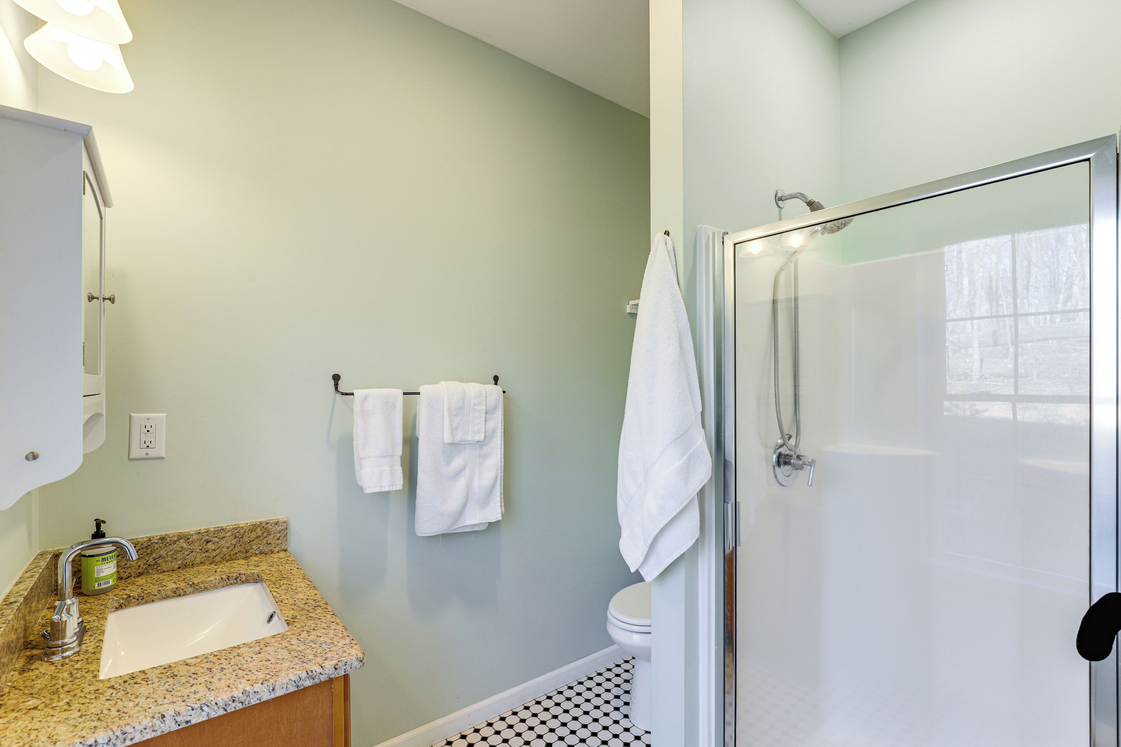 A bathroom with a granite countertop sink, a toilet, a glass shower enclosure, and a towel rack with two white towels.