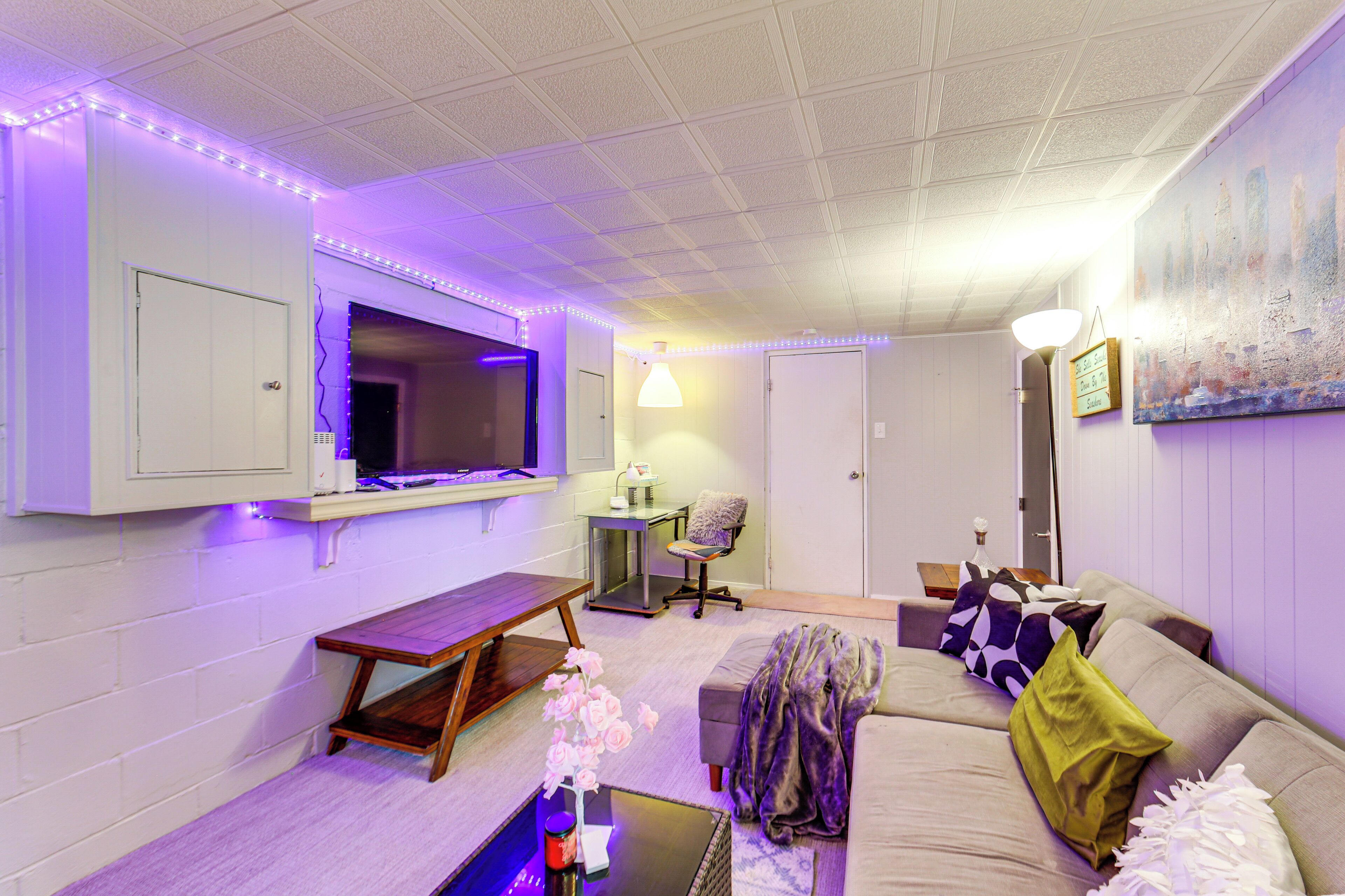 A modern living room with a flat-screen TV, a sofa, a coffee table, and ambient purple lighting.