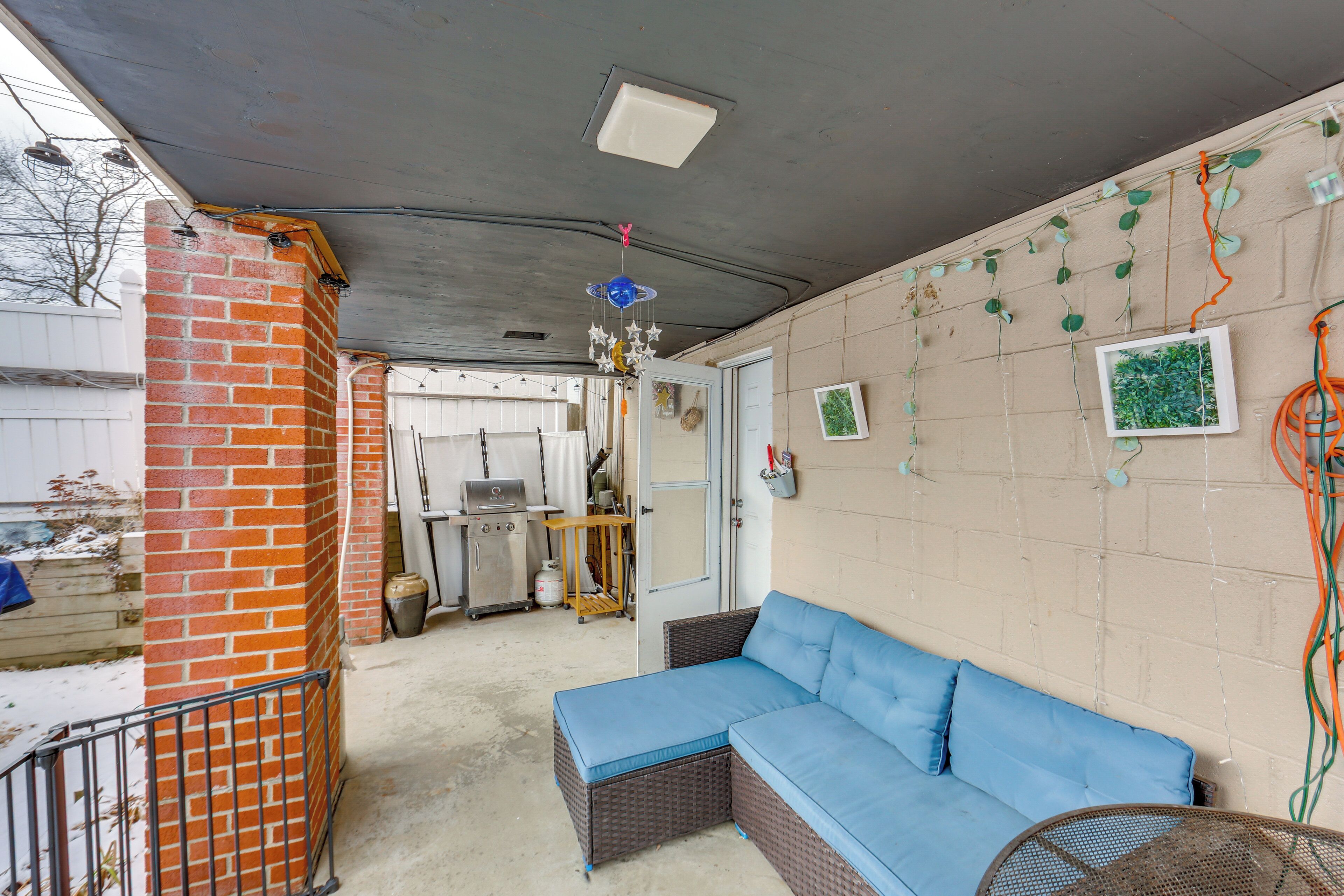 A covered patio area with a blue cushioned seating area, a brick wall, and a ceiling light fixture.