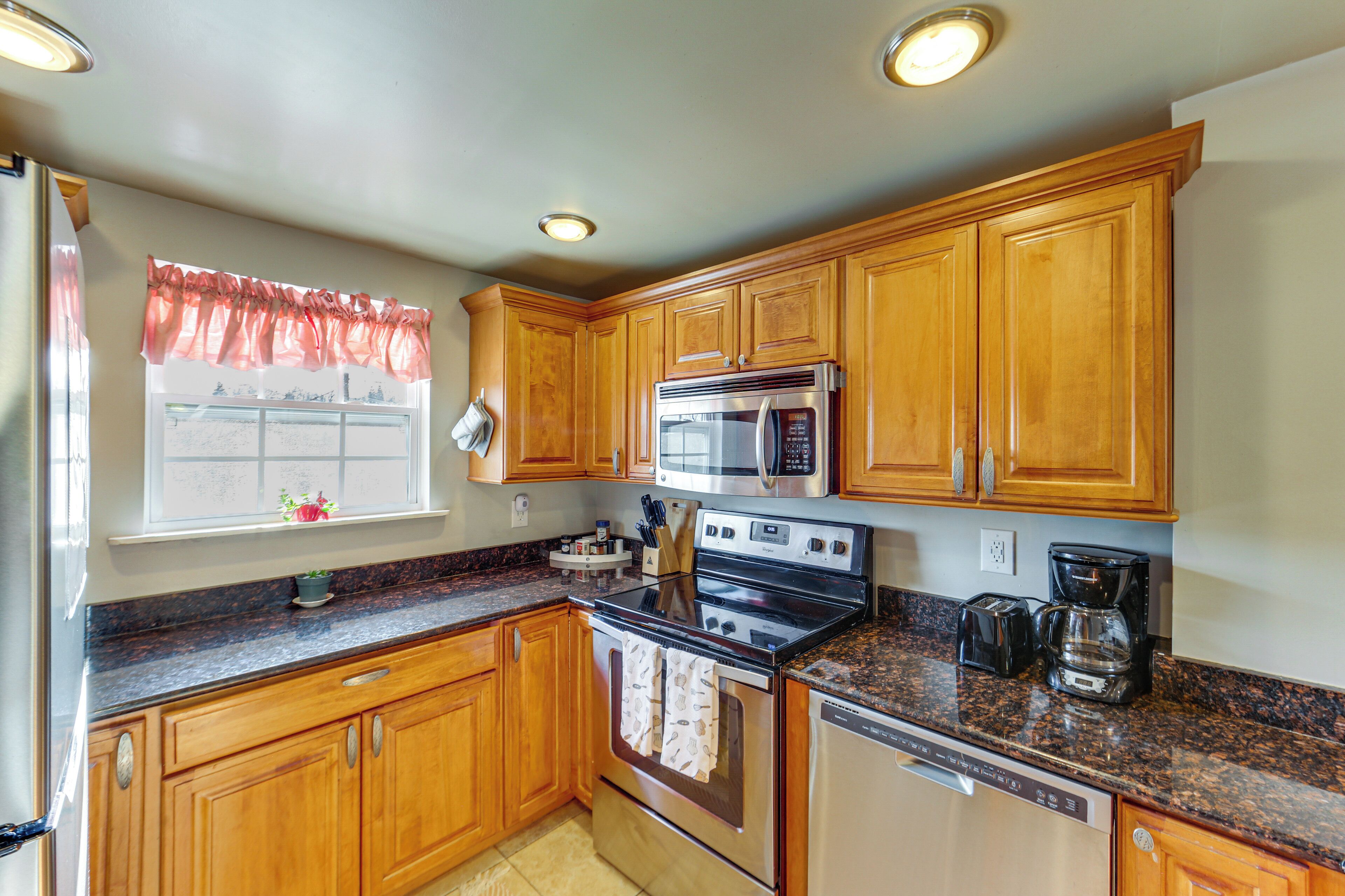 A kitchen with wooden cabinets, stainless steel appliances, granite countertops, and a window with a view.
