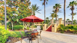 An outdoor patio with a round table and chairs, a red umbrella, and a staircase leading to an upper level. - 9 Mi to Wdw: Resort-style Townhome w/ Pool Access (Davenport)