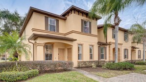A two-story building with a beige facade, multiple windows with shutters, and a landscaped front yard with palm trees and shrubs. - 9 Mi to Wdw: Resort-style Townhome w/ Pool Access (Davenport)