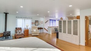 A spacious bedroom with a large bed, a wooden floor, a fireplace, a chair, a wardrobe, and a staircase leading to another room. - Couples Retreat in Lompoc! Studio w/ Lush Garden (Lompoc)