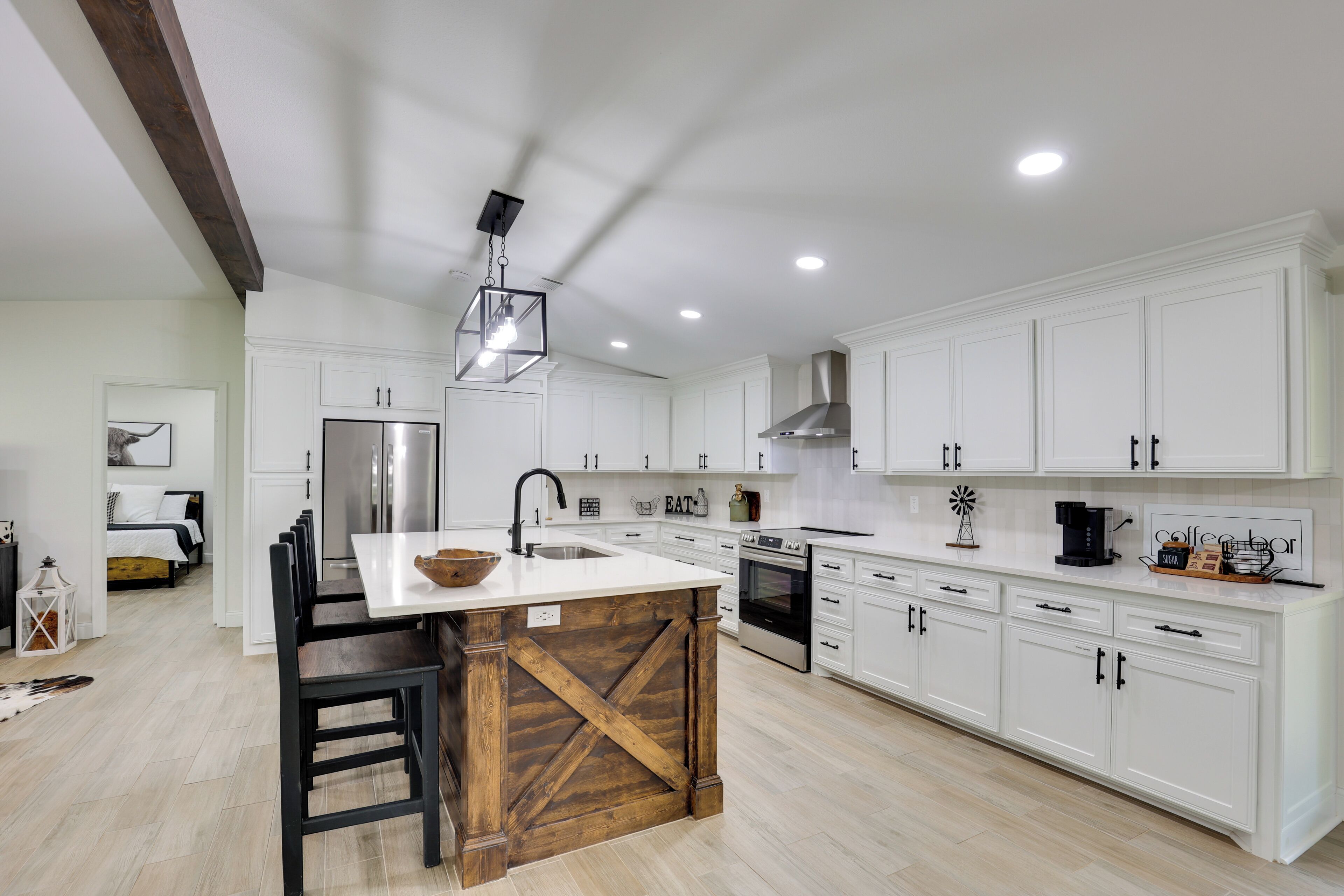 A modern kitchen with white cabinetry, a central island, and a farmhouse-style cross beam.
