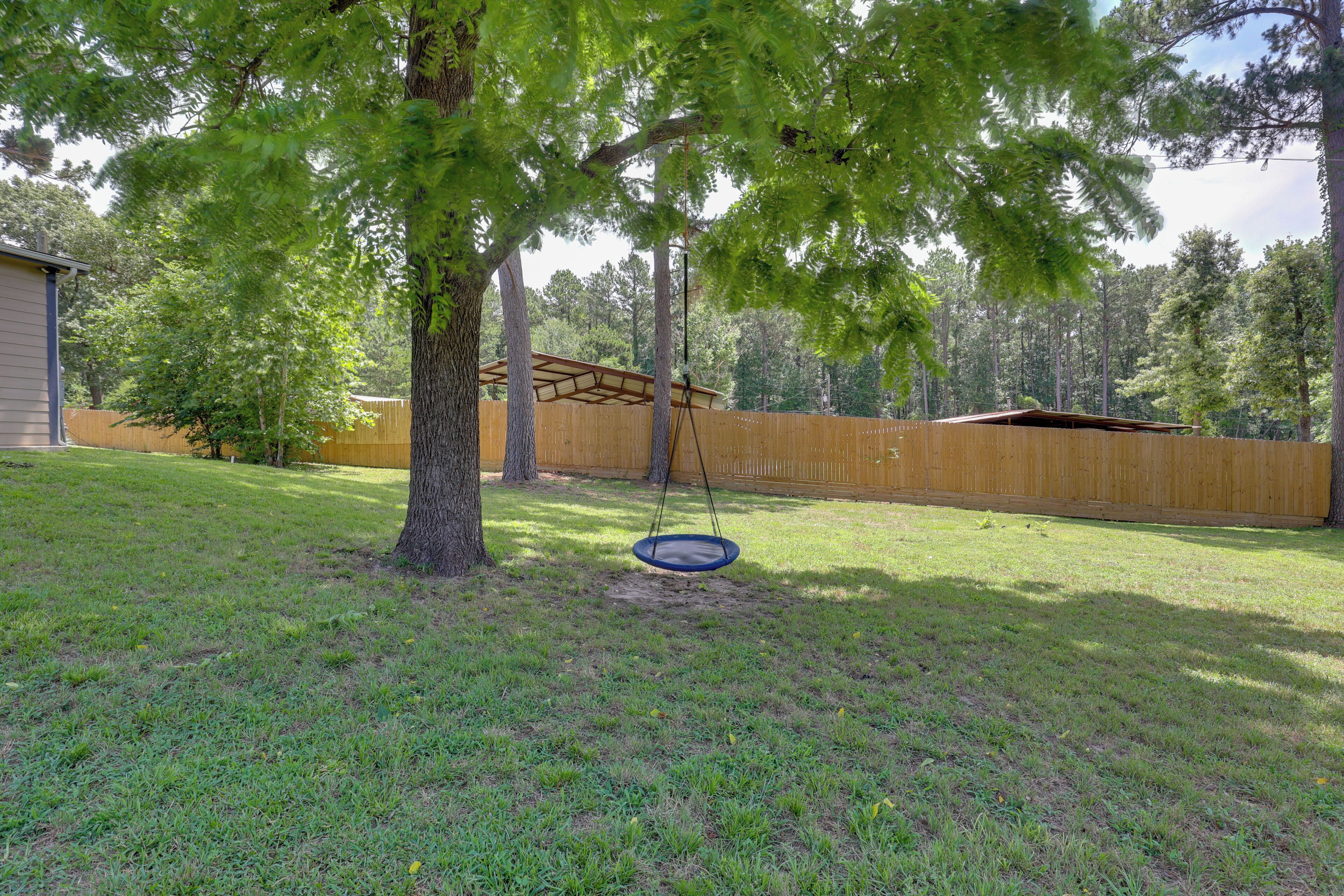 A backyard with a swing set, a wooden fence, and a tree.