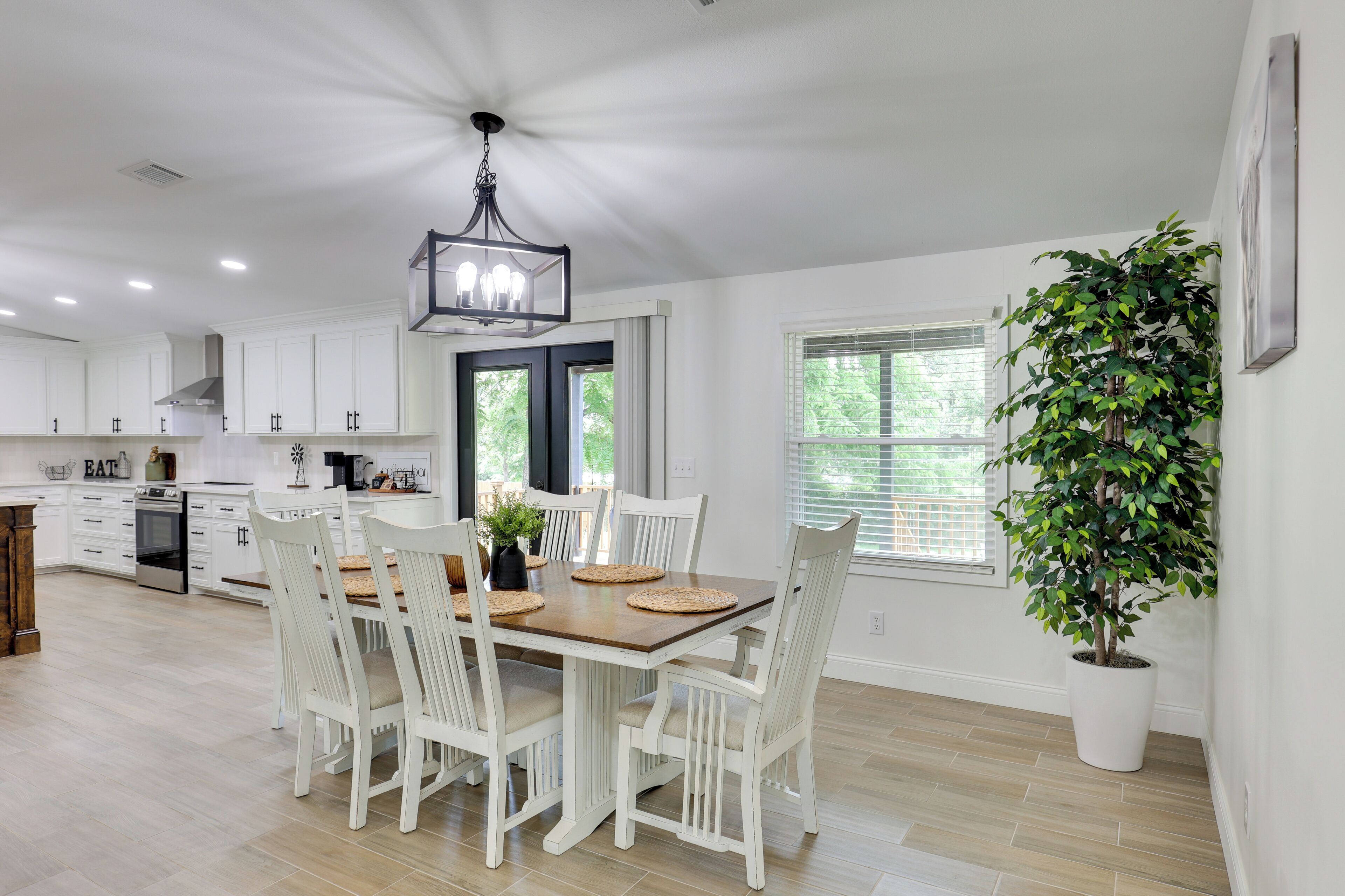 A modern kitchen with white cabinetry, a dining table with chairs, a chandelier, and a potted plant.