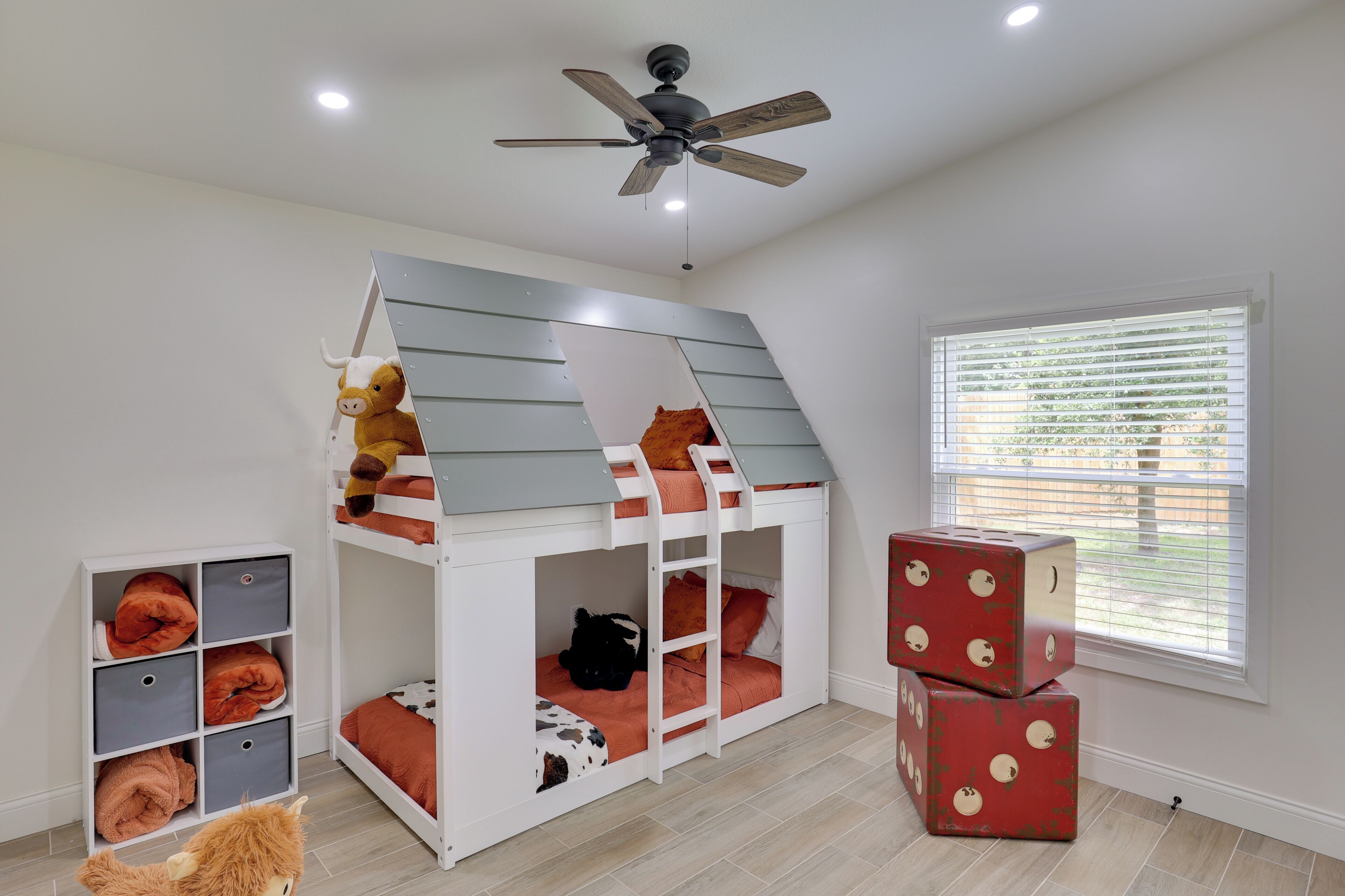 Un lit superposé avec des tiroirs de rangement, un ventilateur de plafond et une fenêtre avec des stores.