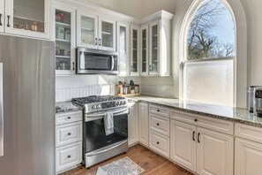 Una cocina con armarios blancos, un refrigerador de acero inoxidable, un microondas, una estufa y un ventanal grande.