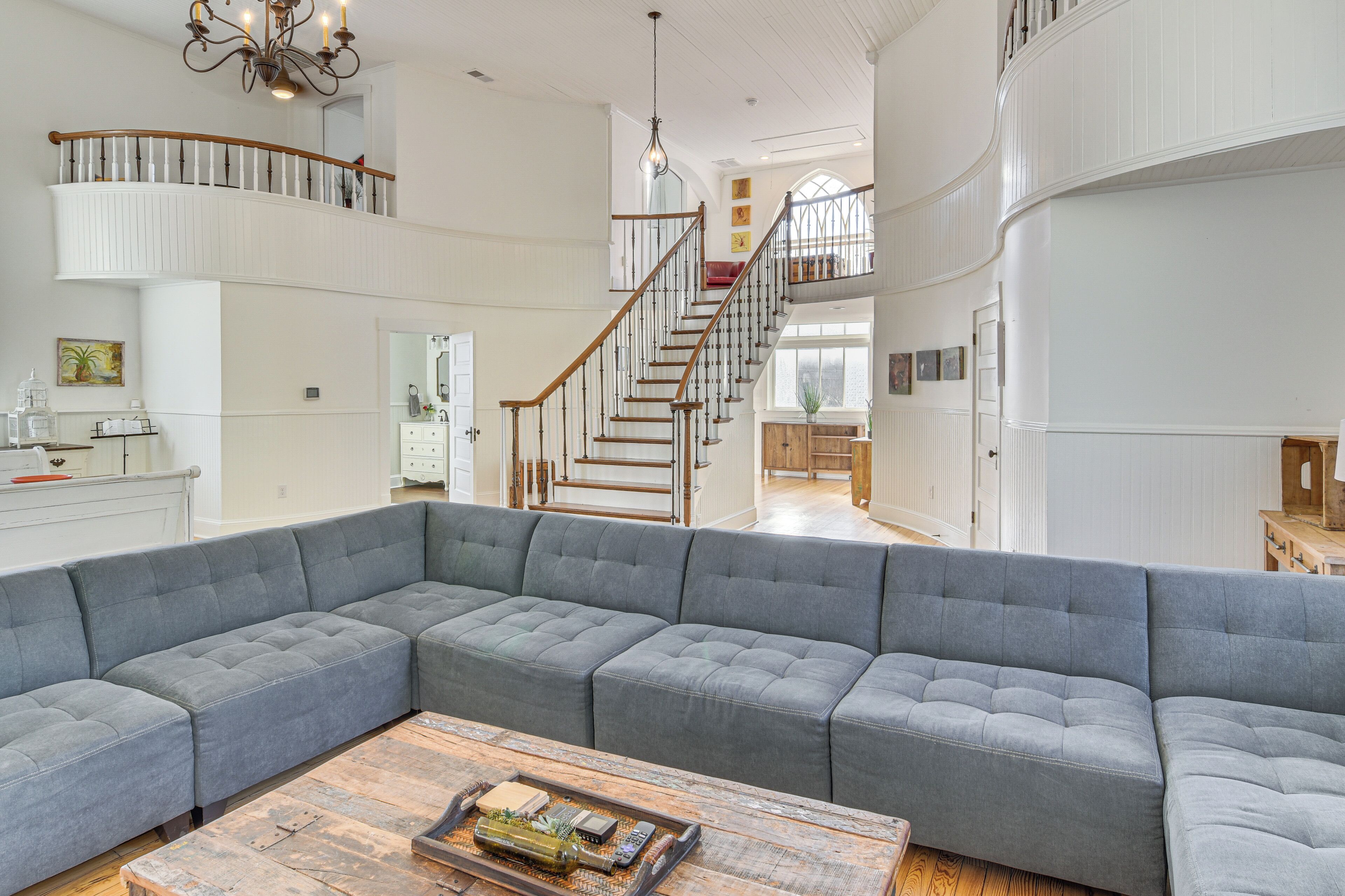 A spacious living room with a large gray sectional sofa, a wooden coffee table, and a staircase leading to an upper level.