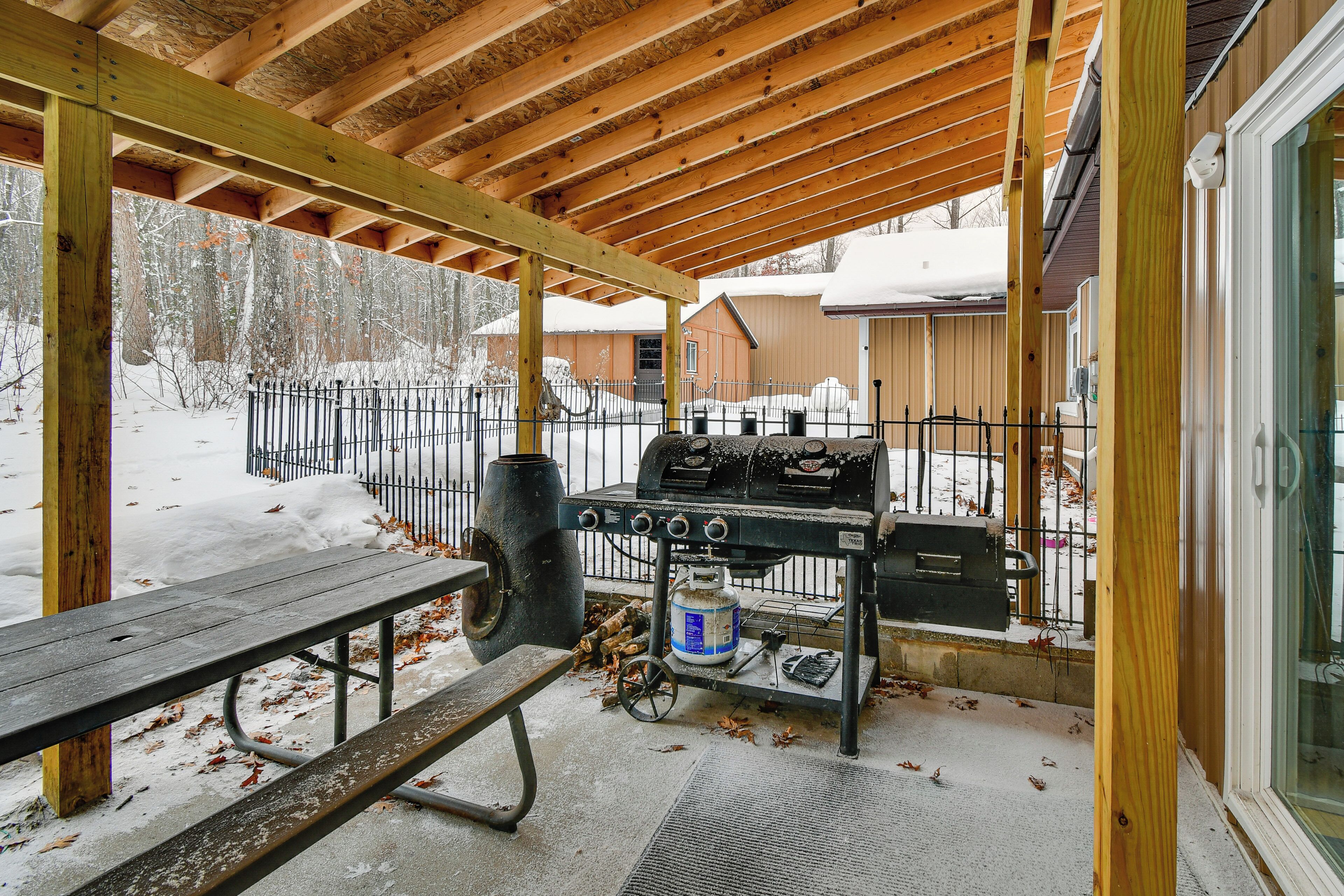 Un patio techado al aire libre con una parrilla, una mesa de picnic y un paisaje cubierto de nieve.