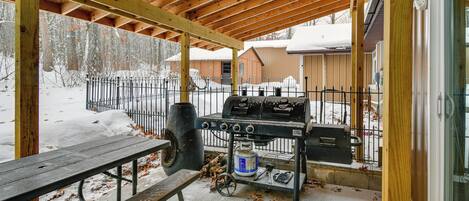 Un patio techado al aire libre con una parrilla, una mesa de picnic y un paisaje cubierto de nieve.