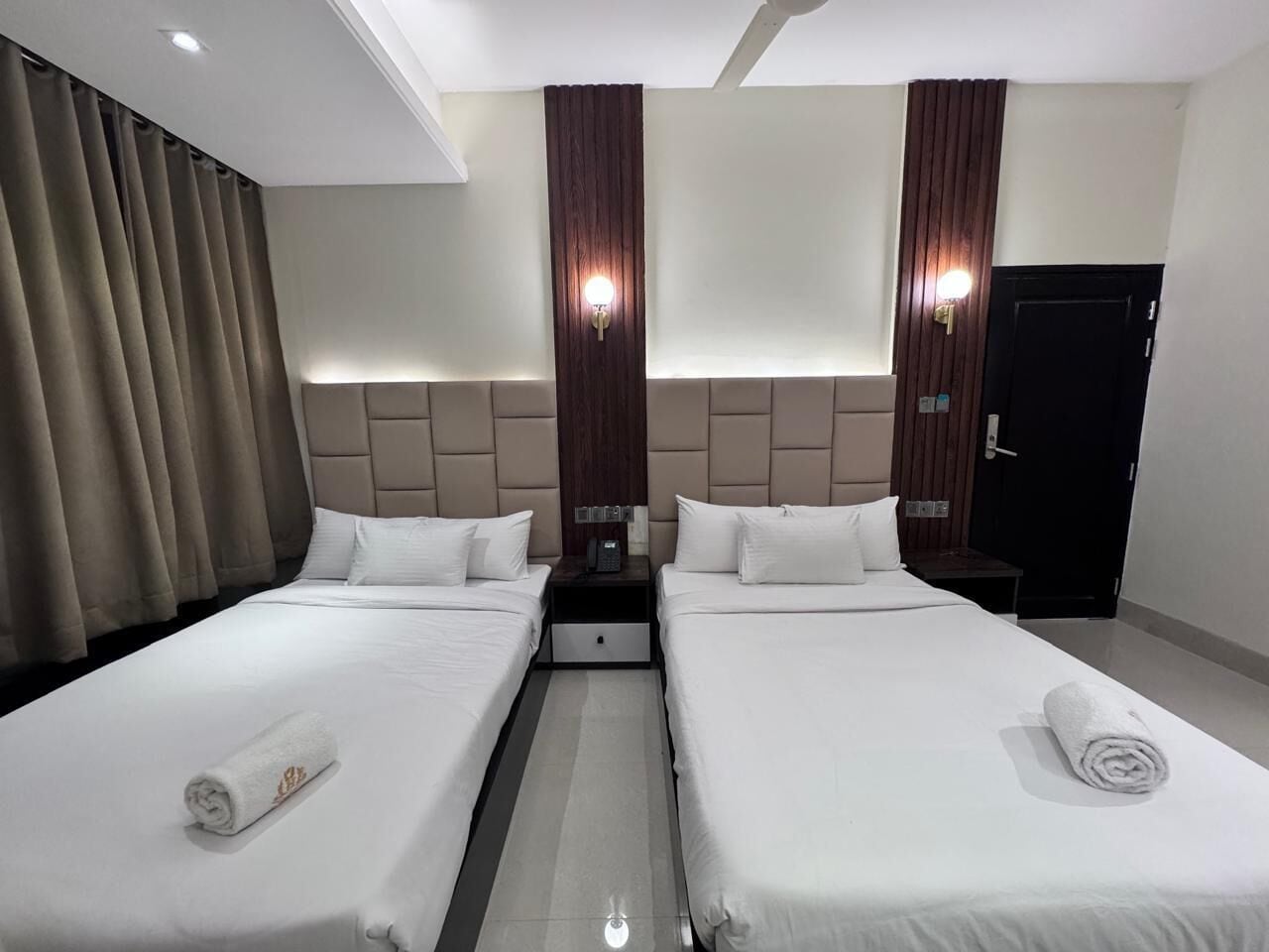 A hotel room with two beds, a nightstand, a wall-mounted phone, and a door.