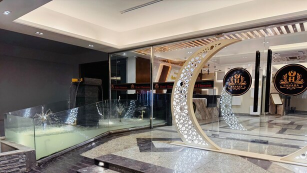 A modern hotel lobby with a glass railing, a water feature, and a reception desk. - Grand Khalifa Hotel Hamama (Sylhet)