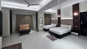 A modern hotel room with a sofa, two single beds, a ceiling fan, and a large mirror. - Grand Khalifa Hotel Hamama (Sylhet)