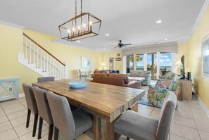 A spacious living area with a wooden dining table, comfortable seating, a staircase, and a view of the outdoors. - DIRECT OCEAN FRONT 5 Bed 6 Bath with Pool (Surfside Beach)