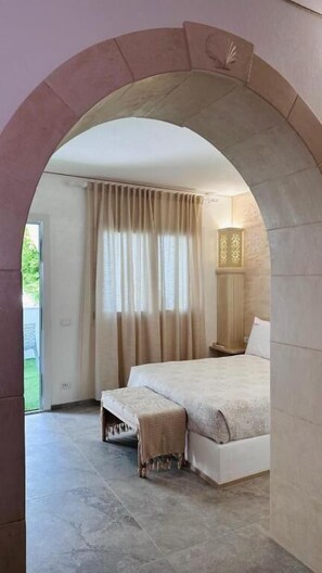 A bedroom with a large bed, a bench, and a window with curtains. - Oasi Cleopatra Luxury suite B&B (Manduria)