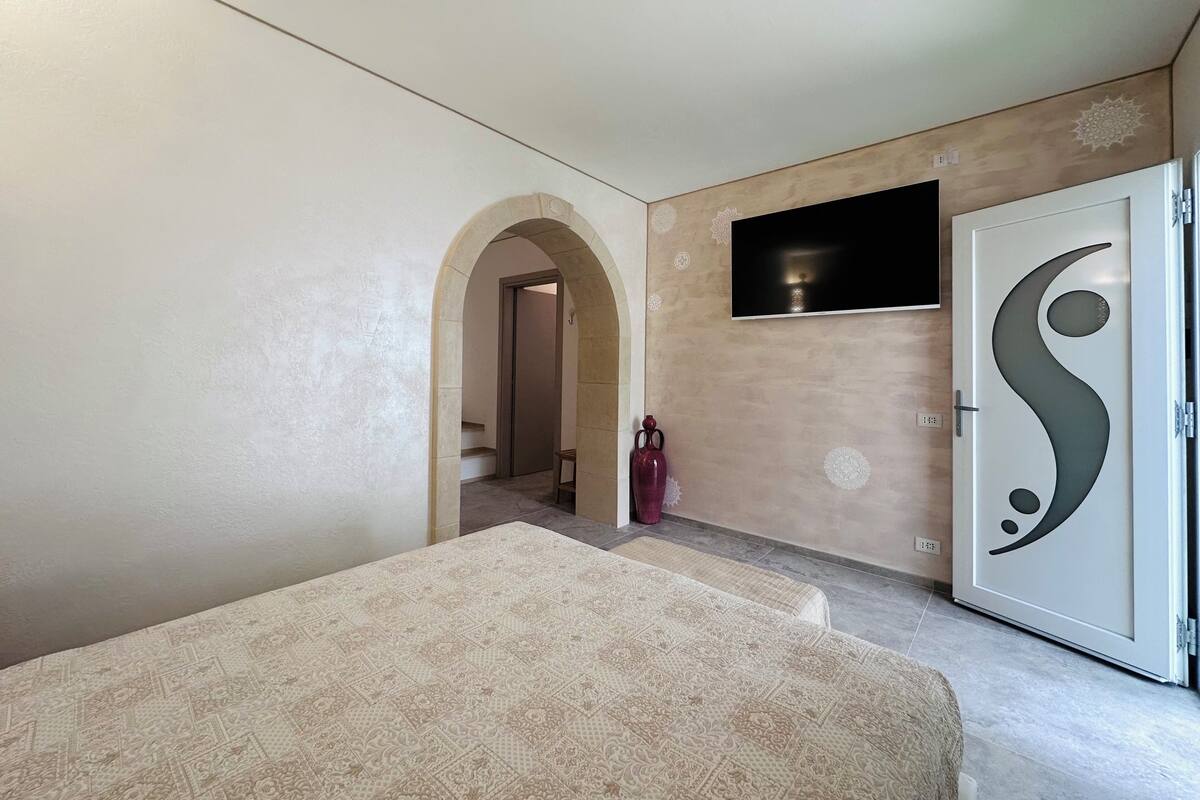 A bedroom with a bed, a TV mounted on the wall, and a door with a decorative design.