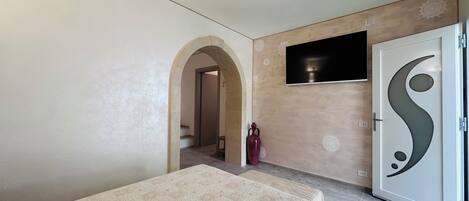 Un dormitorio con cama, televisor montado en la pared y una puerta con detalles decorativos.